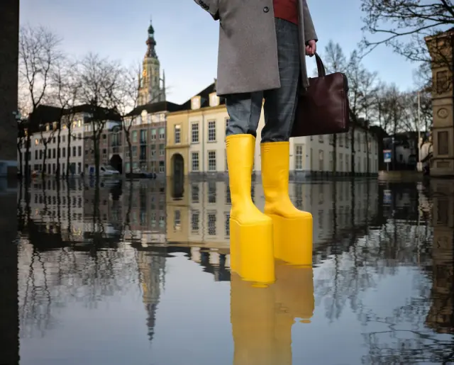 Afgewerkte gele klimaatlaarzen met hoge zolen in het campagnebeeld met de Grote Kerk van Breda en een weerspiegeling in water
