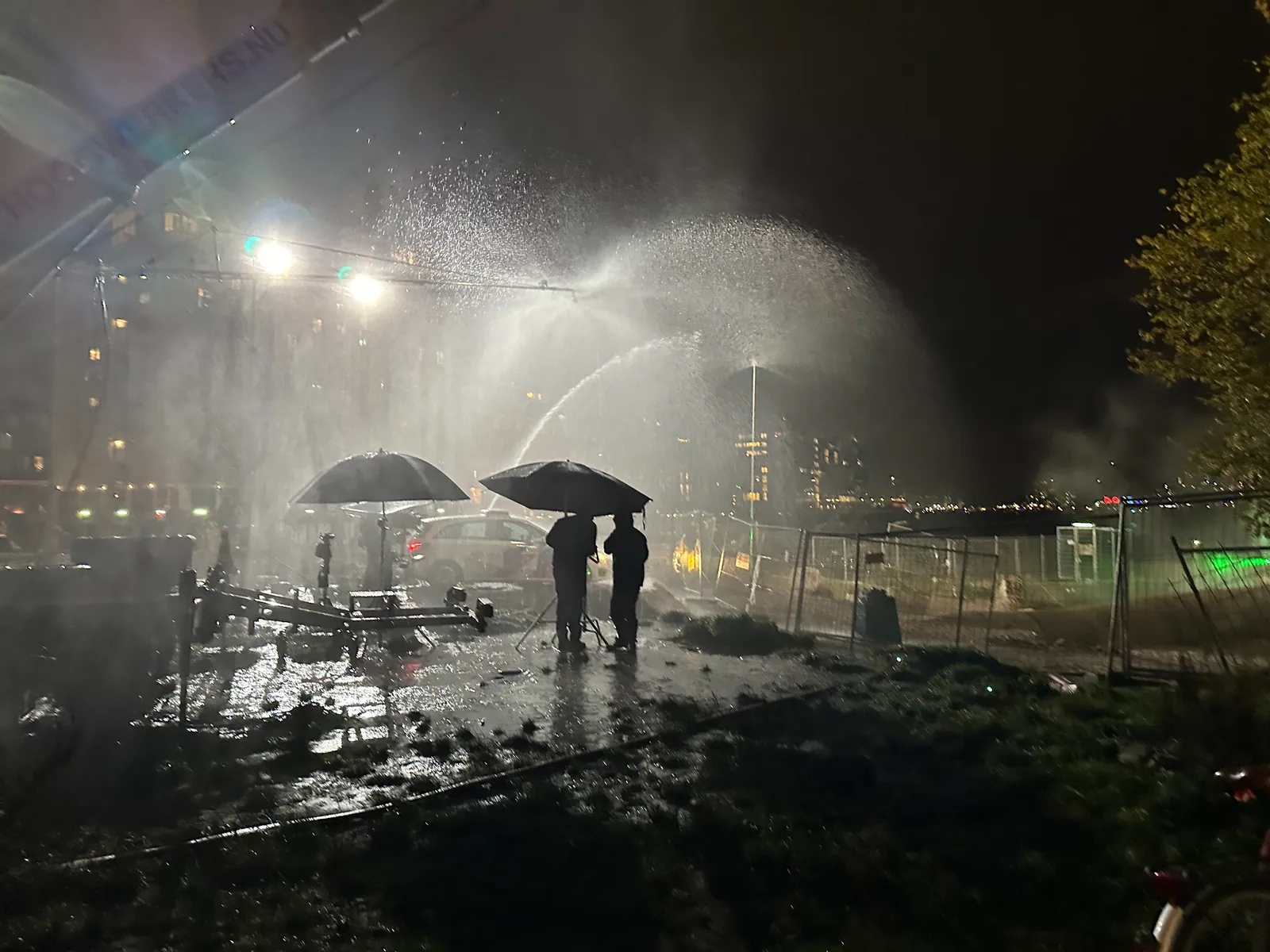 Crew onder paraplu’s in een verlichte regenopstelling voor Amsterdamned II