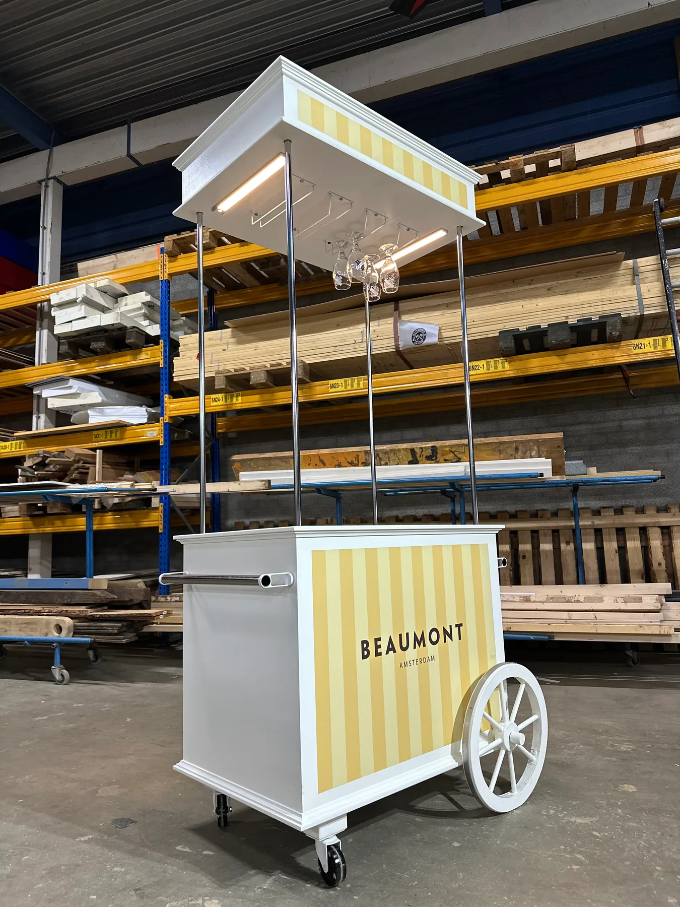 Complete geel-witte Beaumont-cocktailkar met groot wiel, verlicht dak en hangende glazen in de werkplaats