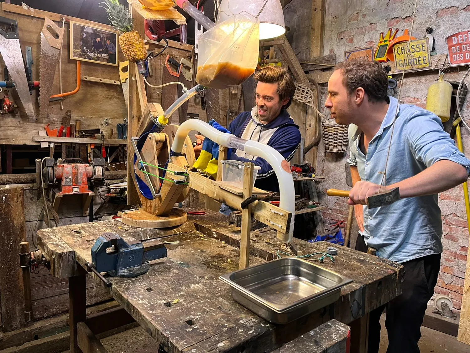 De presentatoren bedienen de mechanische poepmachine tijdens de opnamen van De Proefkeuken in de kleine werkplaats