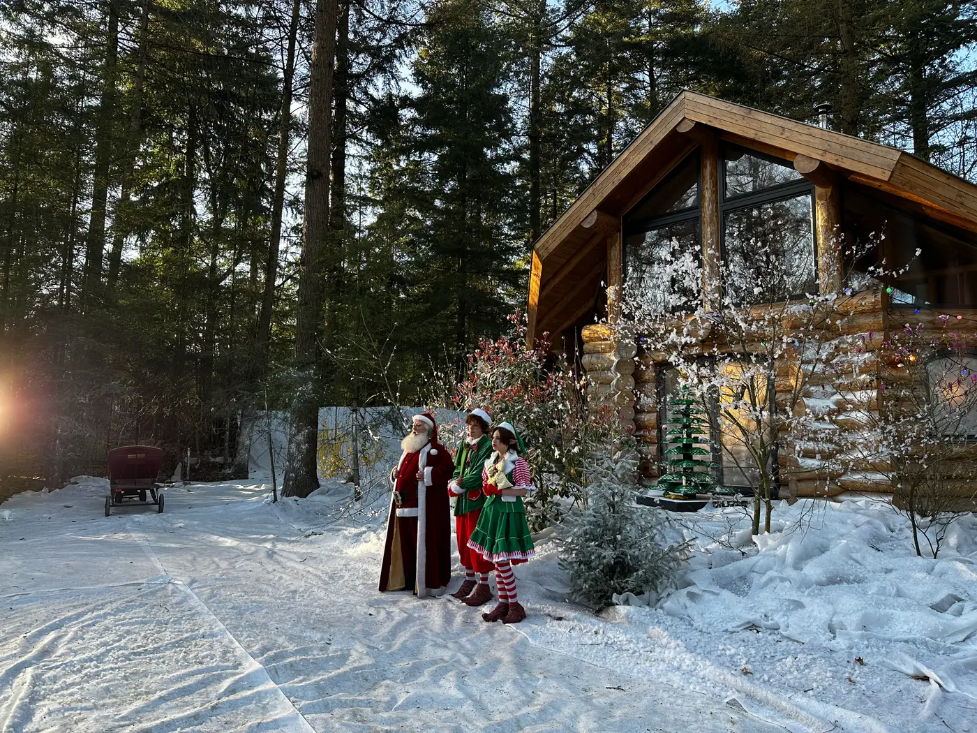 Kerstman en twee figuren in elfenkostuum voor de besneeuwde blokhut van De Grote Sinterklaasfilm 2026